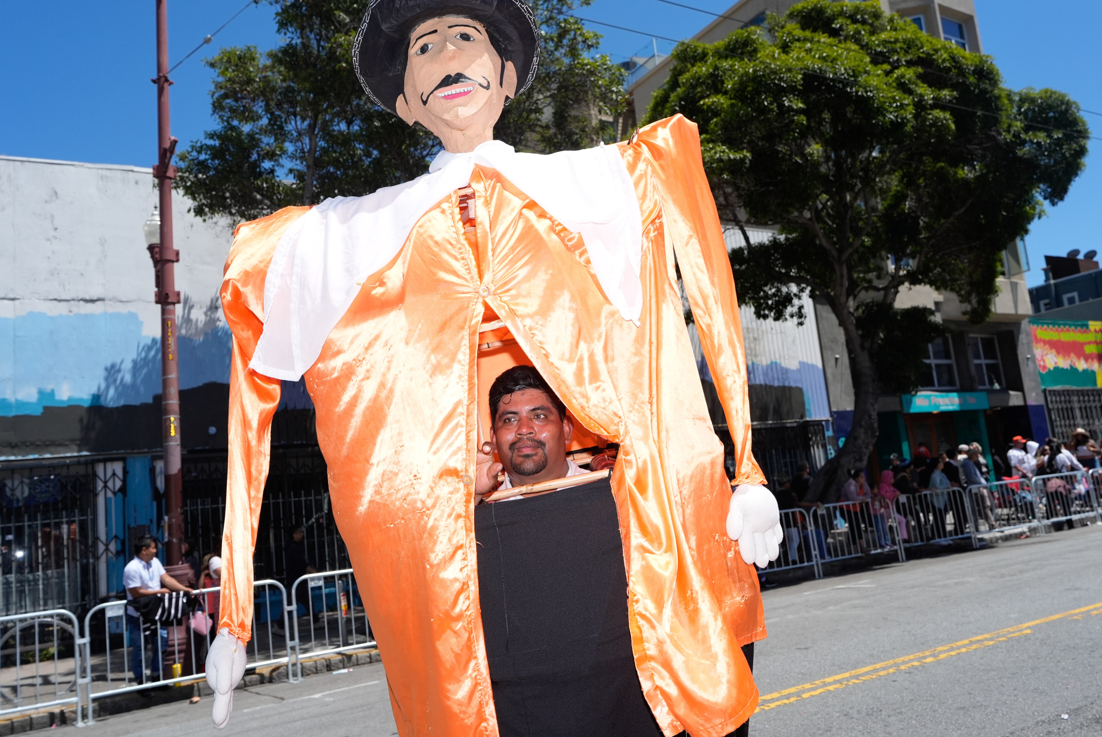 A man inside a large and brightly colored puppet costume manuevers it along a parade route.