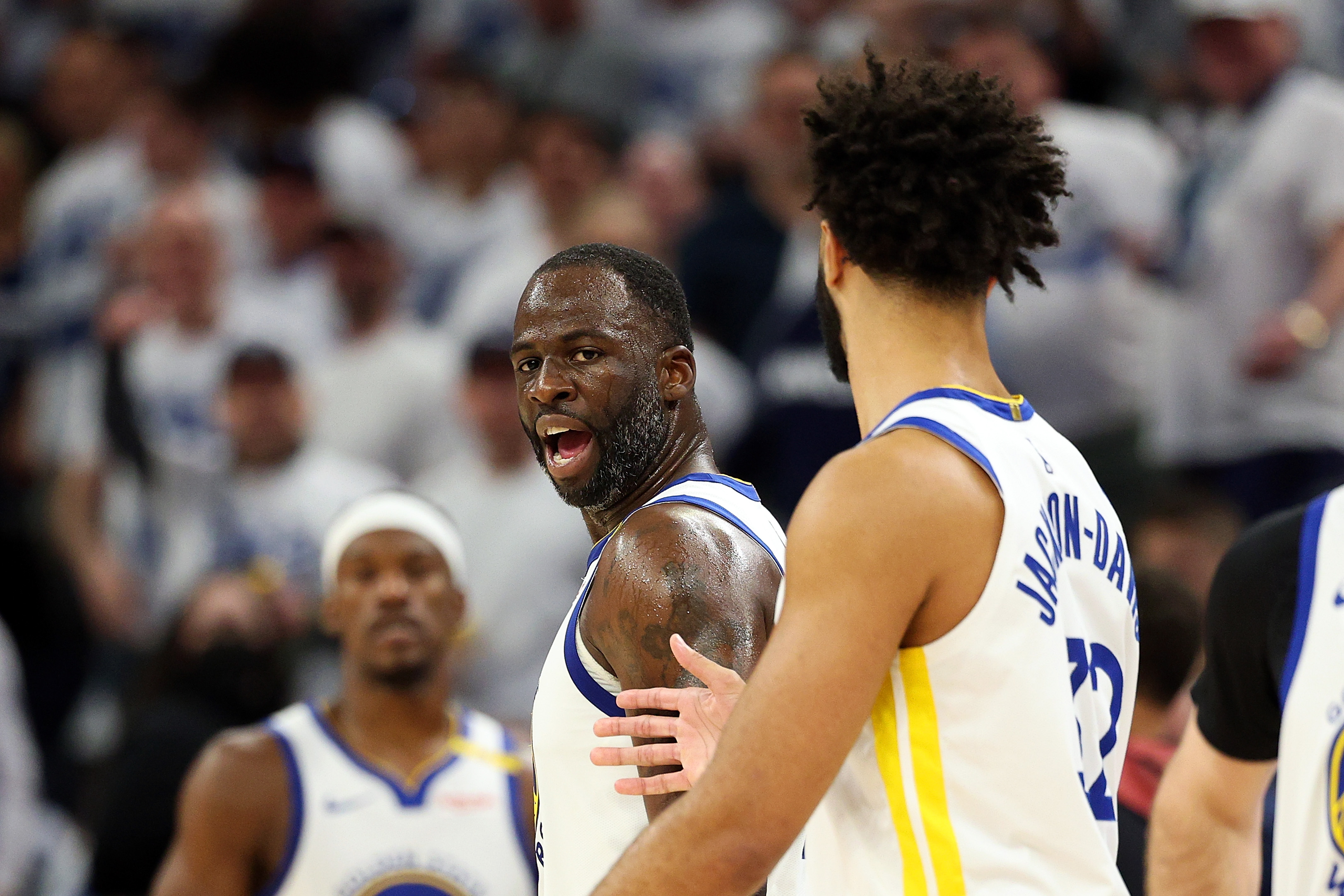 The image shows two basketball players in white jerseys, engaged in an intense moment on the court. One player is expressing strong emotion.
